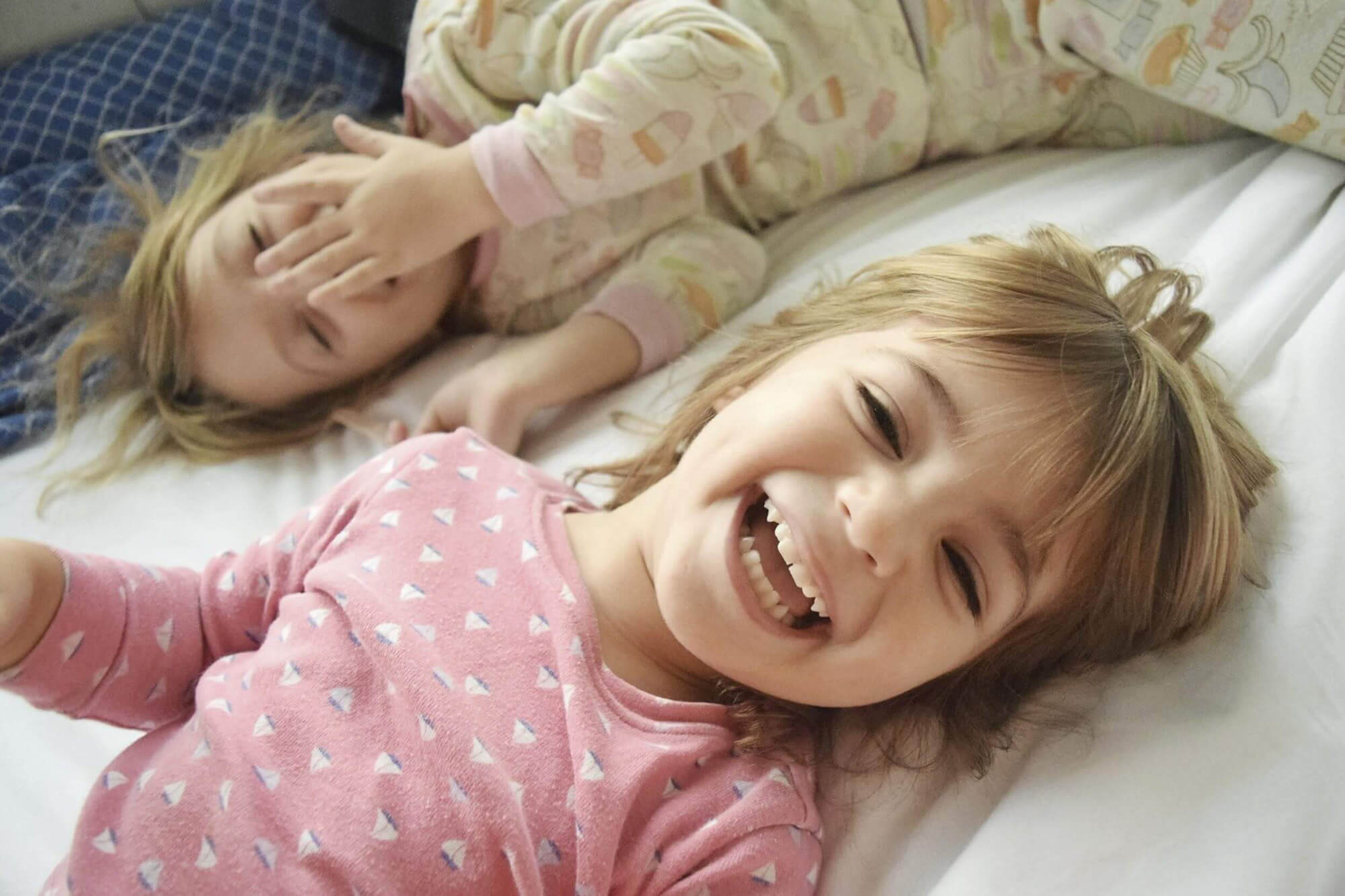 Two Laughing Little Girls on Bed