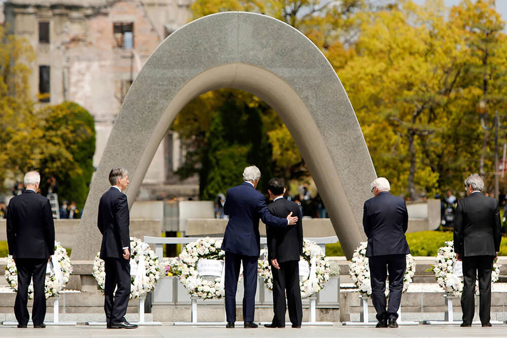 john kerry puts his arm around Japan's foreign minister at the Hiroshima Peace Memorial